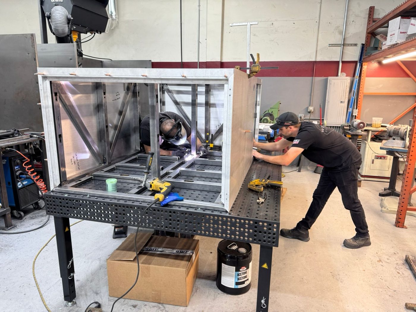 Welding the TAP enclosure while a technician fits the side panel