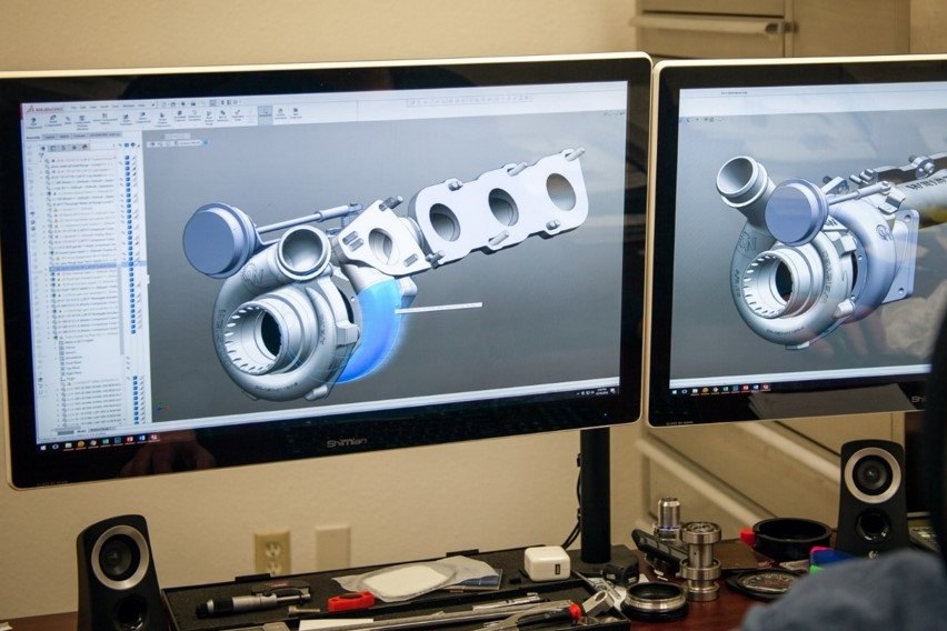 Turbocharger and manifold assembly modeled in CAD on dual monitors